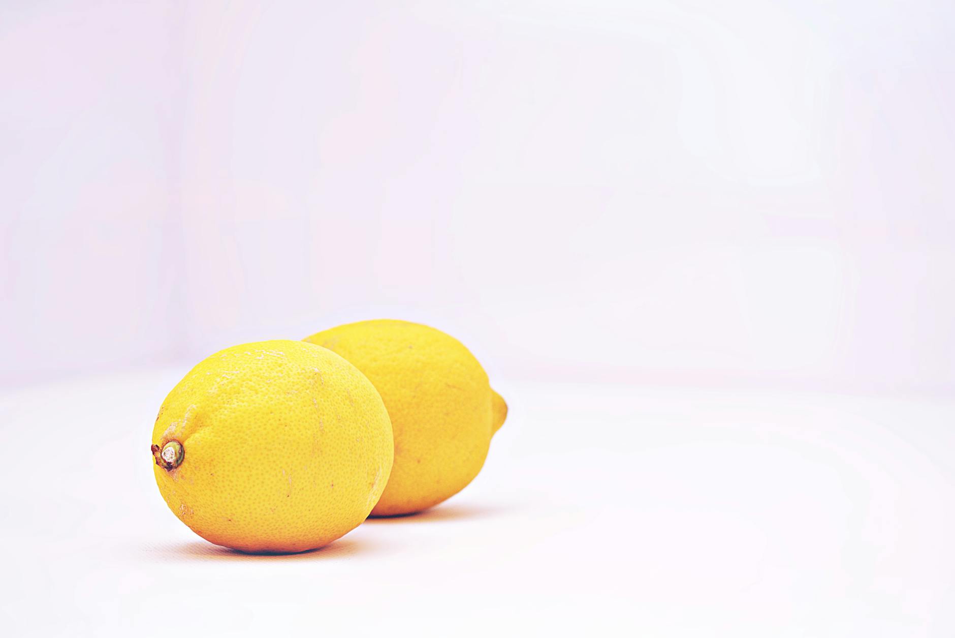 Hand holding a fresh lemon against a soft pink background with additional lemons nearby, symbolizing the natural support of lemon clitoral vibrators