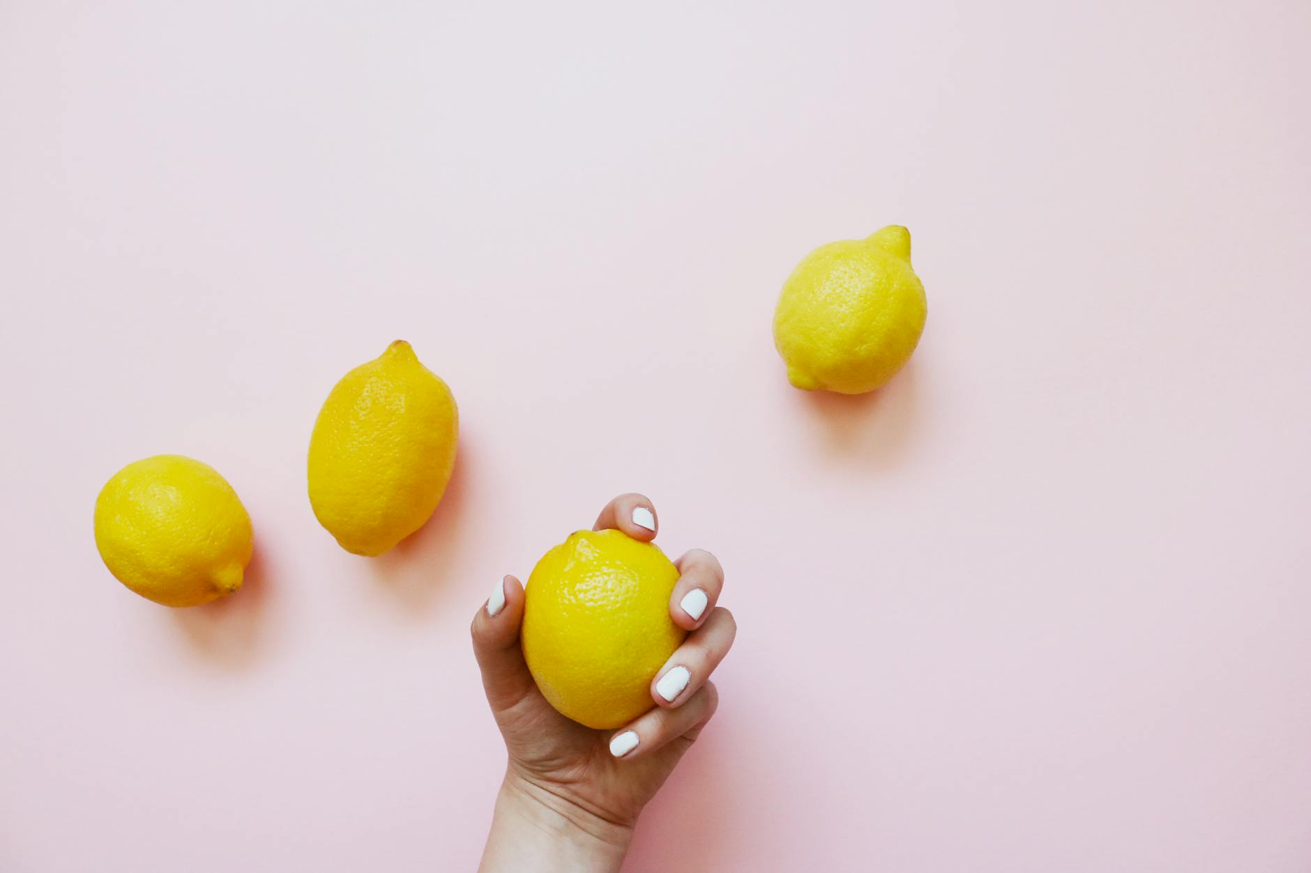 A hand holding a lemon on a soft pink background, symbolizing natural pleasure and aging.