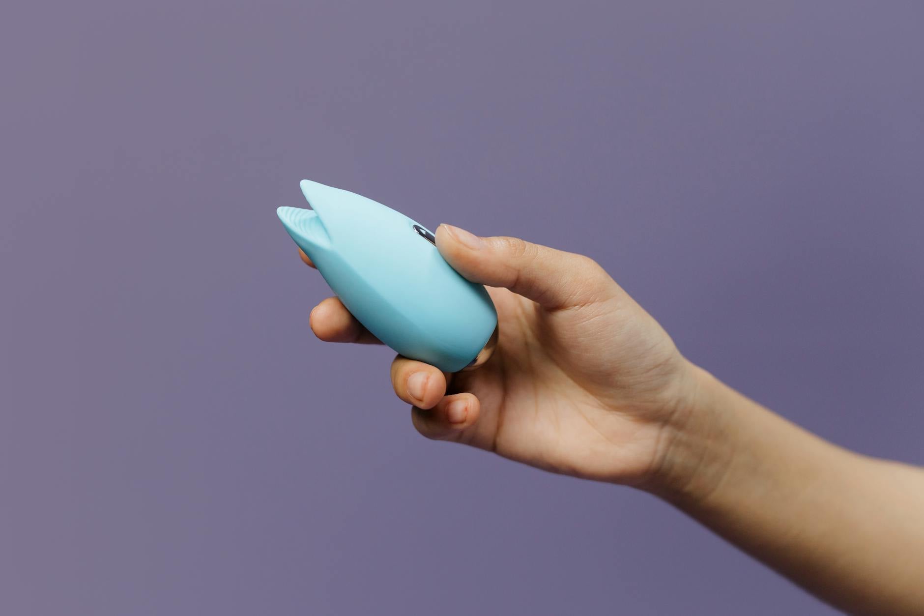 A hand holding a lemon-colored silicone vibrator against a purple background, symbolizing gentle sexual wellness recovery