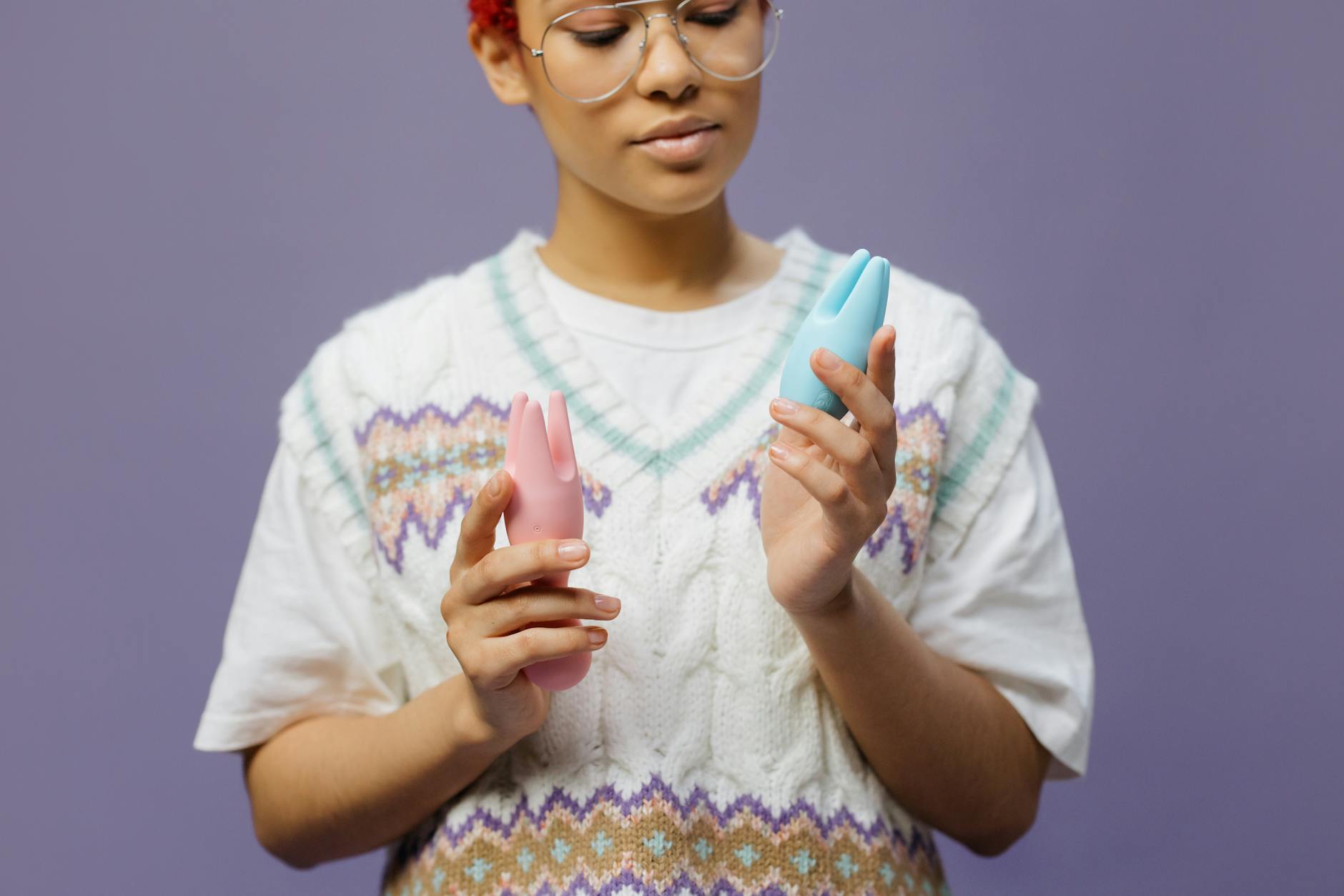 Woman contemplating holding a blue and pink silicone vibrator, considering pleasure after time away.
