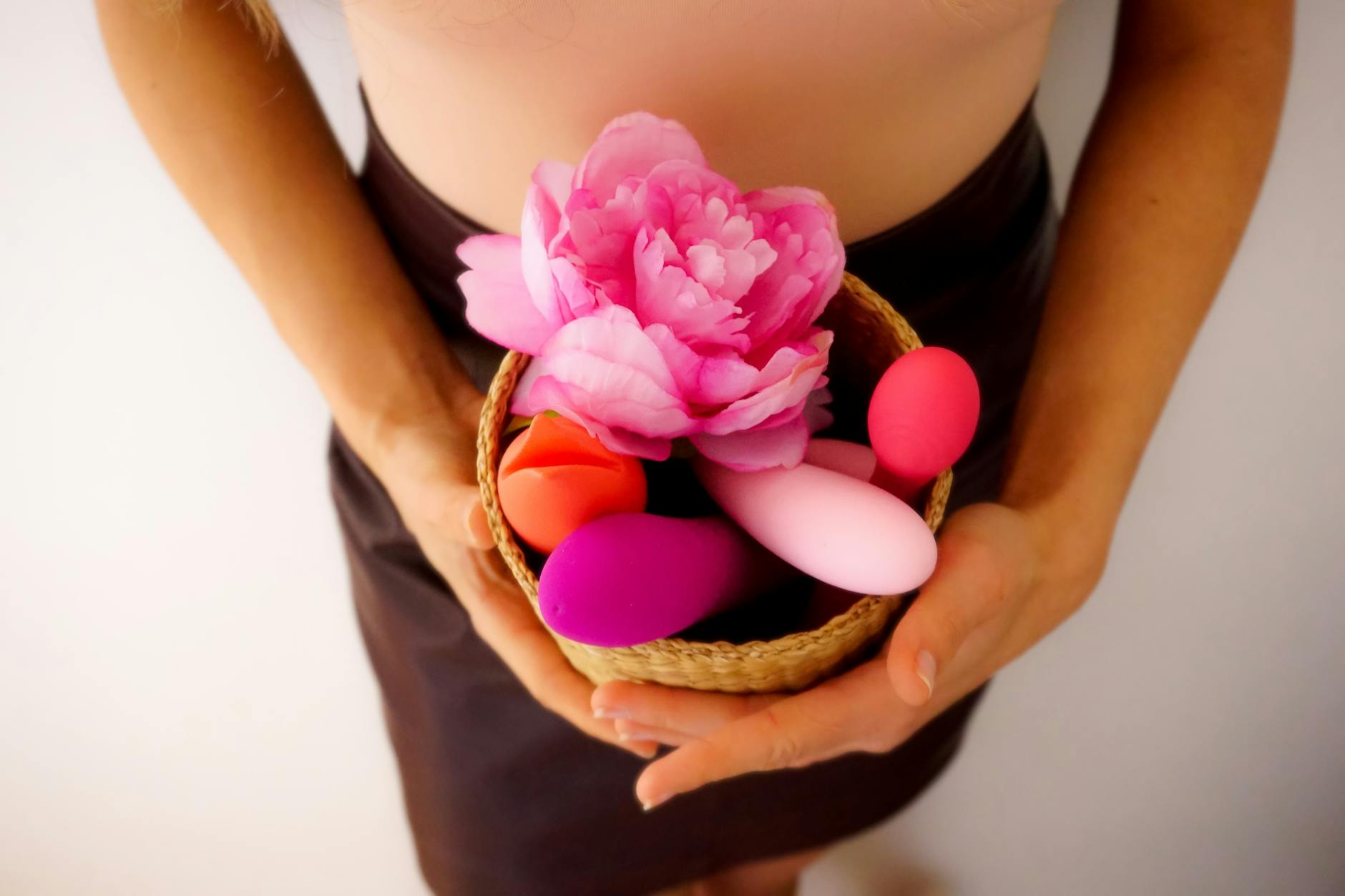 A basket containing colorful vibrators and a pink flower, representing pleasure-focused intimacy without performance pressure.